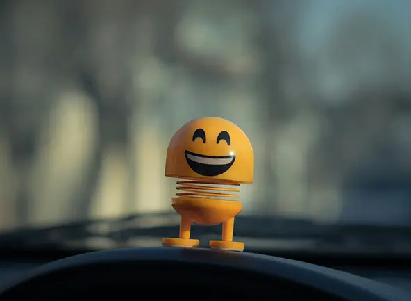 Figurină zâmbitoare pe bordul unei mașini – simbol al stării de bine și al bucuriei unui zâmbet sănătos